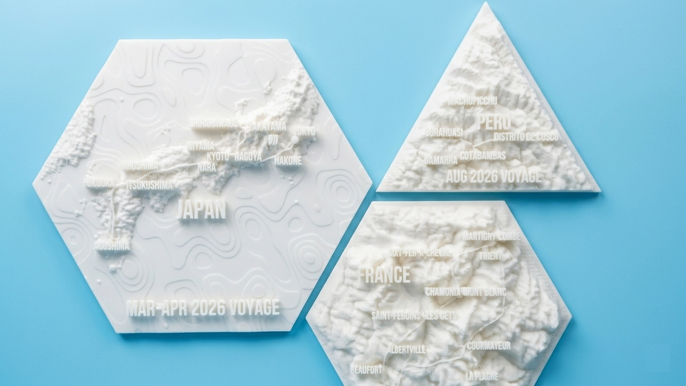 Three Voyaprint models on a blue background: a hexagonal Japan plaque alongside two triangular country reliefs.